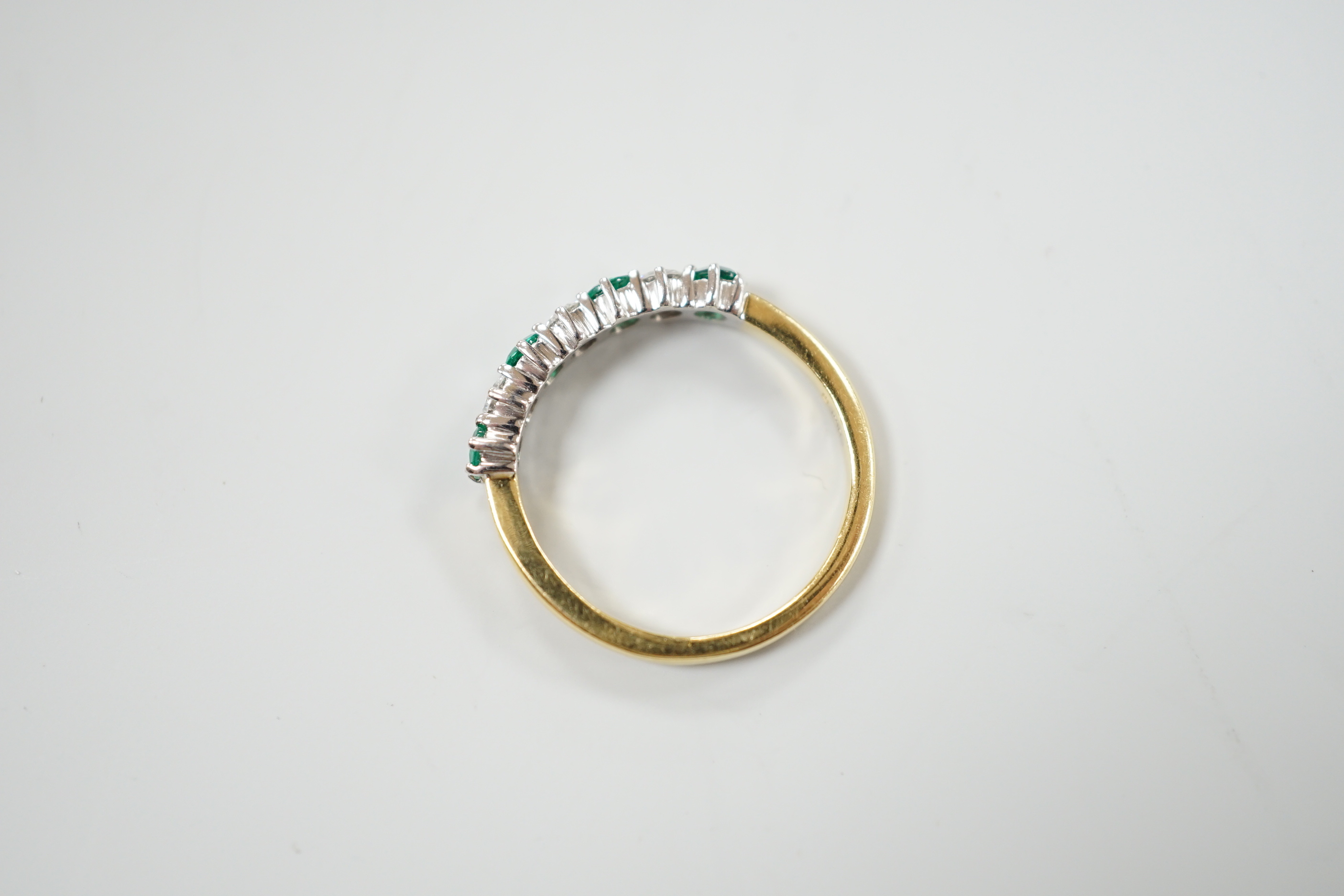 A modern 18ct gold, four stone emerald and three stone diamond set half hoop ring, size M, gross weight 2.9 grams.